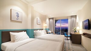 A hotel room with two beds, a desk, a chair, a TV, and a large window with a view. - Coralina Hotel (Tuy Hoa)