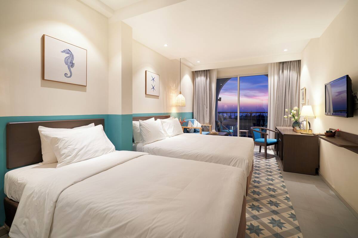 Une chambre d’hôtel avec deux lits, un bureau, une chaise, une télévision et une grande fenêtre donnant sur un beau paysage.