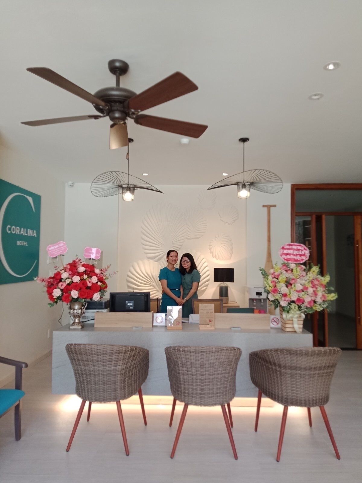 A reception area with a desk, two wicker chairs, a ceiling fan, and decorative wall art.