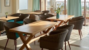 A spacious dining area with high ceilings, a ceiling fan, and large windows with curtains. Tables and wicker chairs are arranged for dining. - Coralina Hotel (Tuy Hoa)
