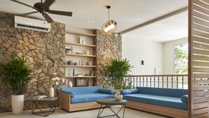 A modern living room with a stone wall, blue sofa, and a ceiling fan. - Coralina Hotel (Tuy Hoa)