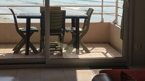 En balkon med et bord og stole, havudsigt og en rød pude.