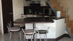 Et moderne køkken med en central ø, barstole, en mikroovn og en trappe.