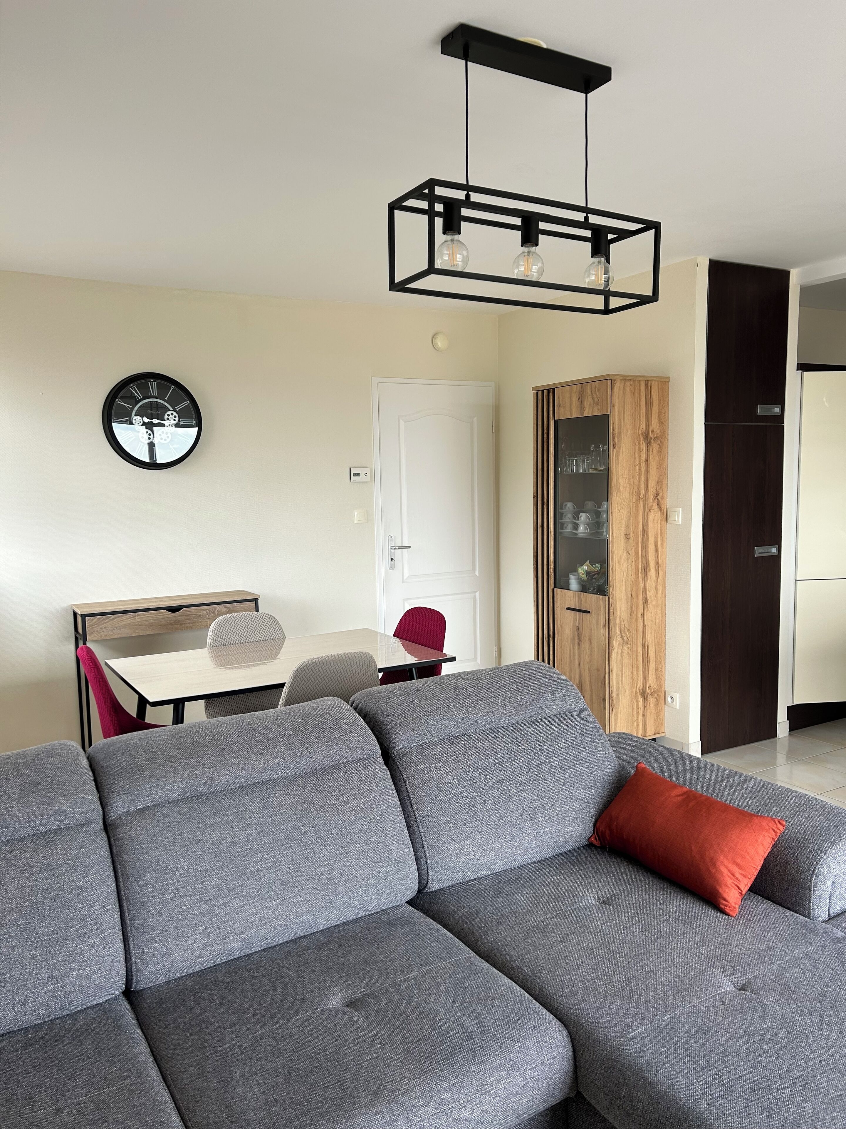 Una sala de estar moderna con un sofá modular, una mesa de comedor con sillas y una zona de cocina al fondo.