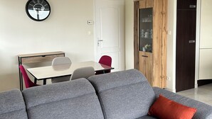En moderne stue med en hjørnesofa, et spisebord med stole og et køkken i baggrunden.