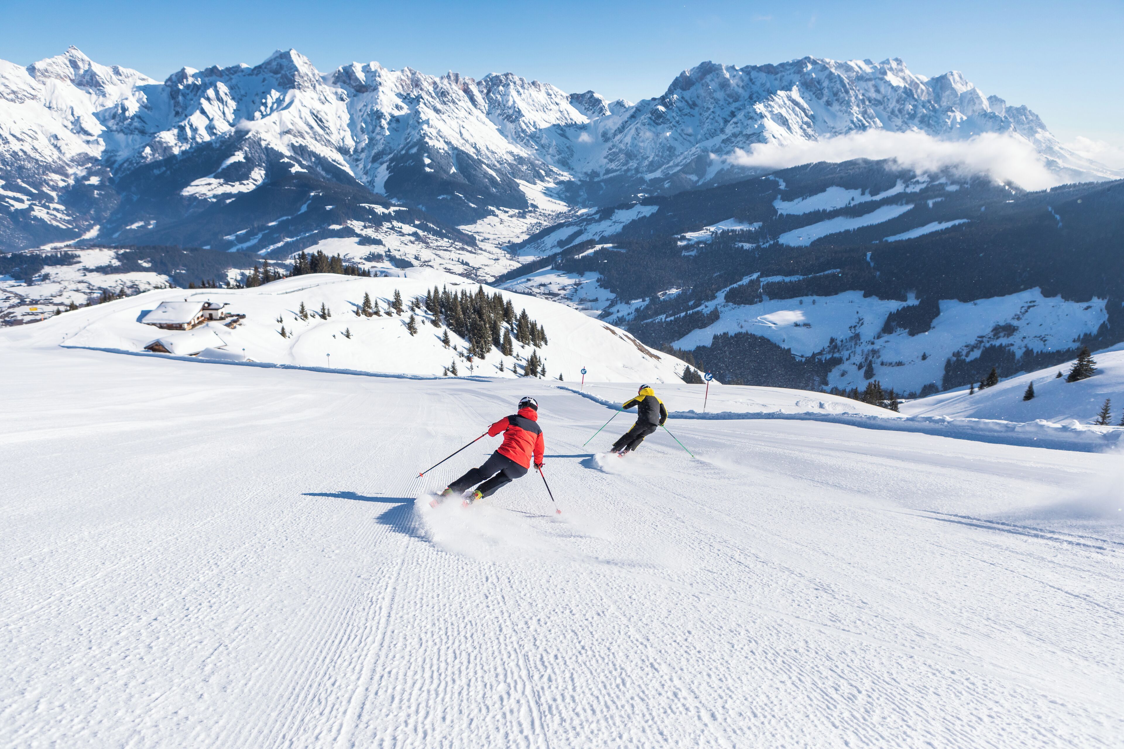 Ein verschneiter Skipisten mit Skifahrern und einem Berg im Hintergrund.