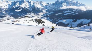 Ein verschneiter Skipisten mit Skifahrern und einem Berg im Hintergrund.