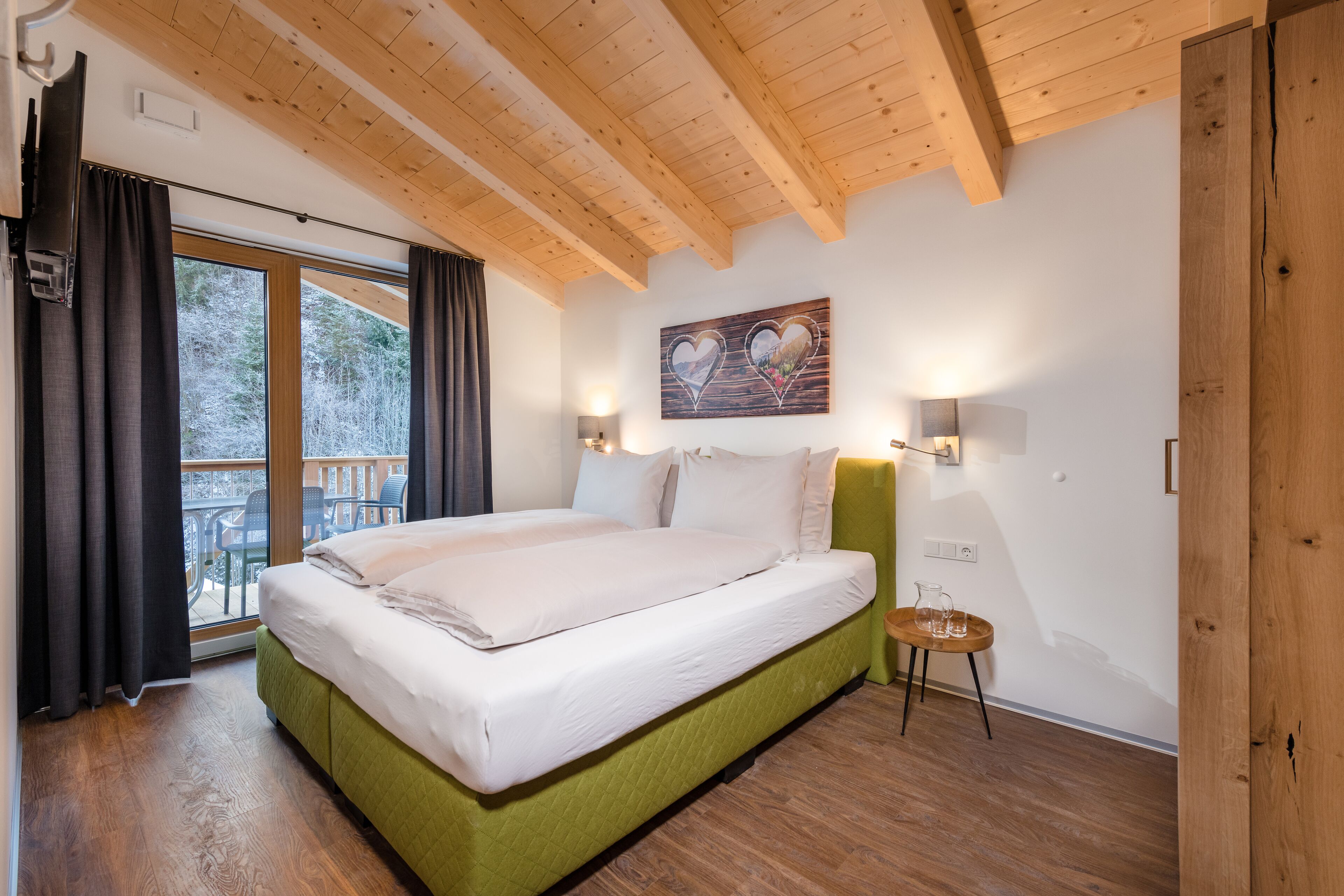 Ein Schlafzimmer mit einem großen Bett, Holzbalkendecke, einem Balkon mit Vorhängen und einem Gemälde an der Wand.