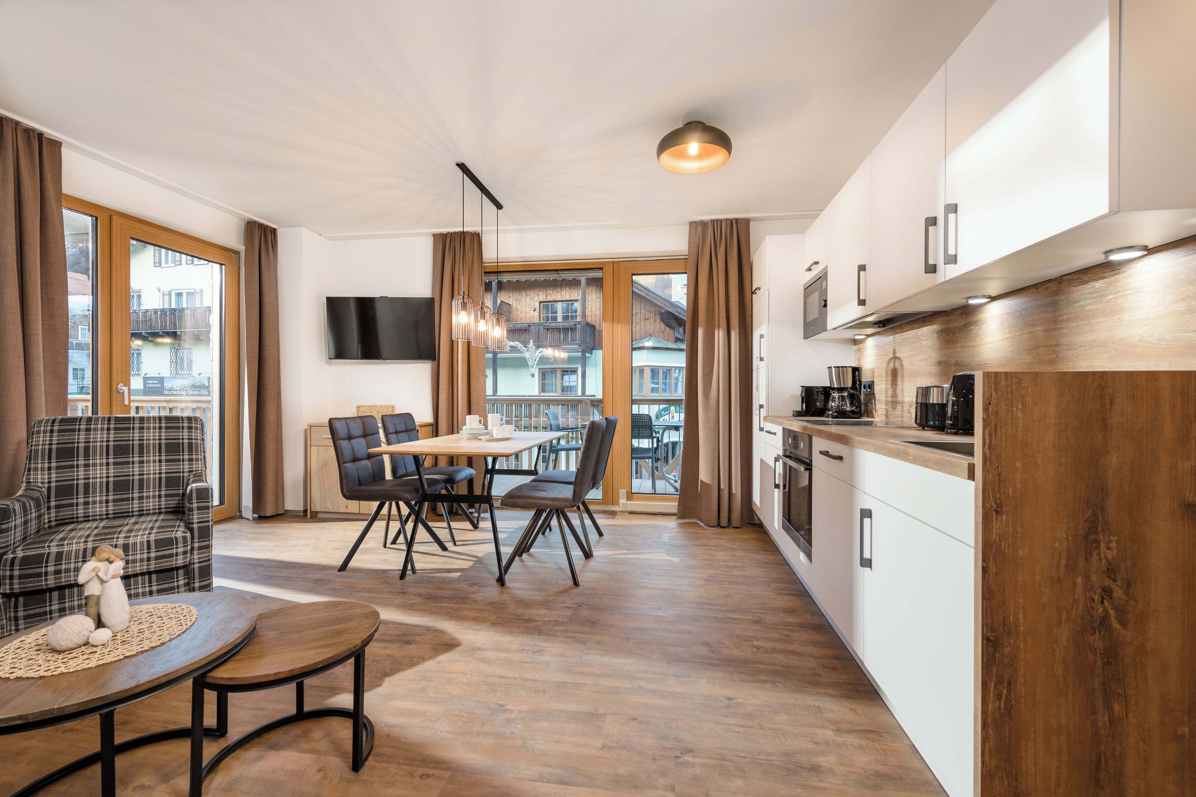 Una sala de estar moderna con un sofá, una mesa de comedor y sillas. Hay una zona de cocina con armarios y un televisor montado en la pared.