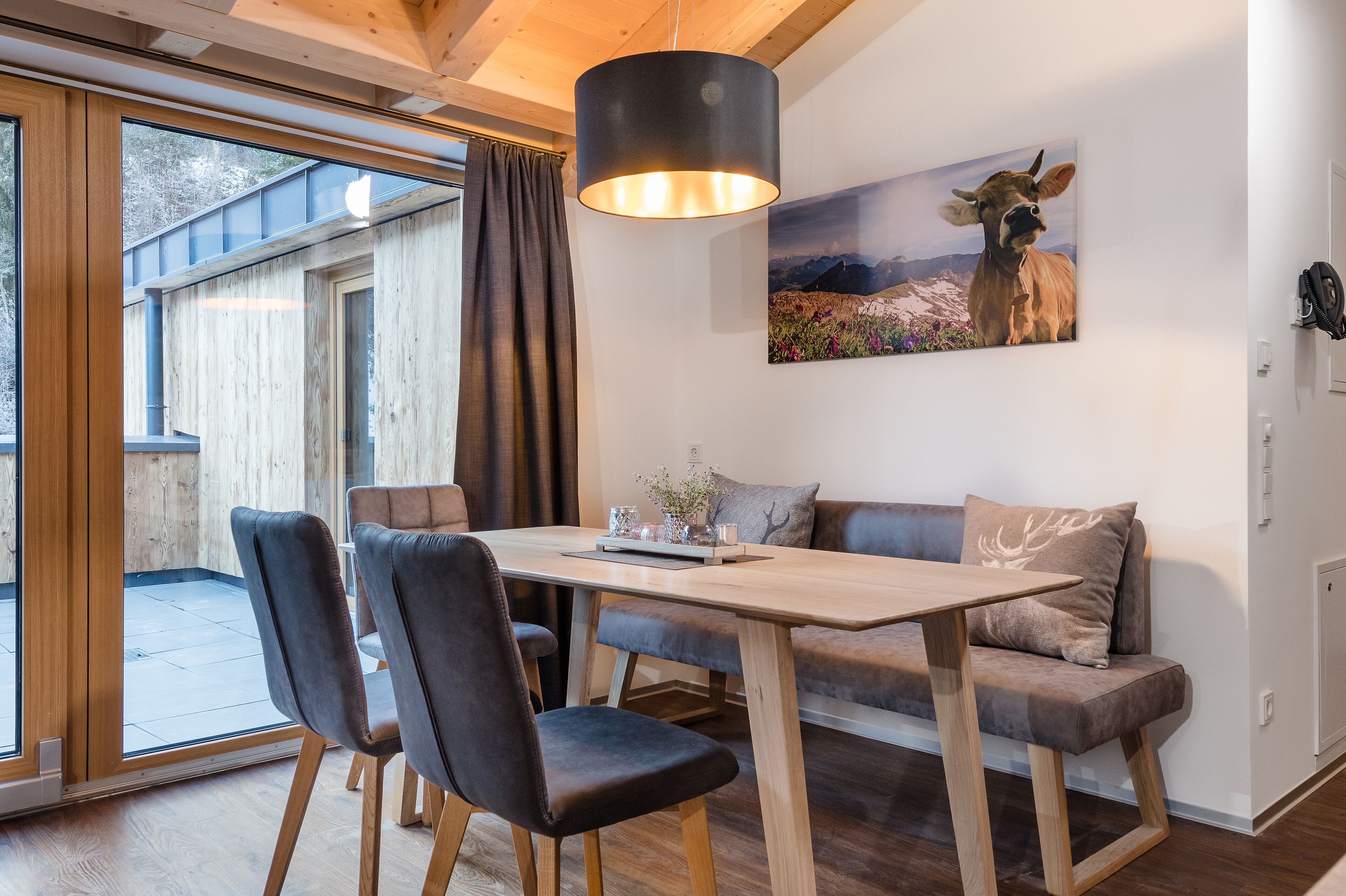 Un interior moderno con una mesa de comedor de madera, dos sillas, un sofá y una lámpara colgante.