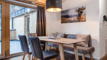 Un interior moderno con una mesa de comedor de madera, dos sillas, un sofá y una lámpara colgante.