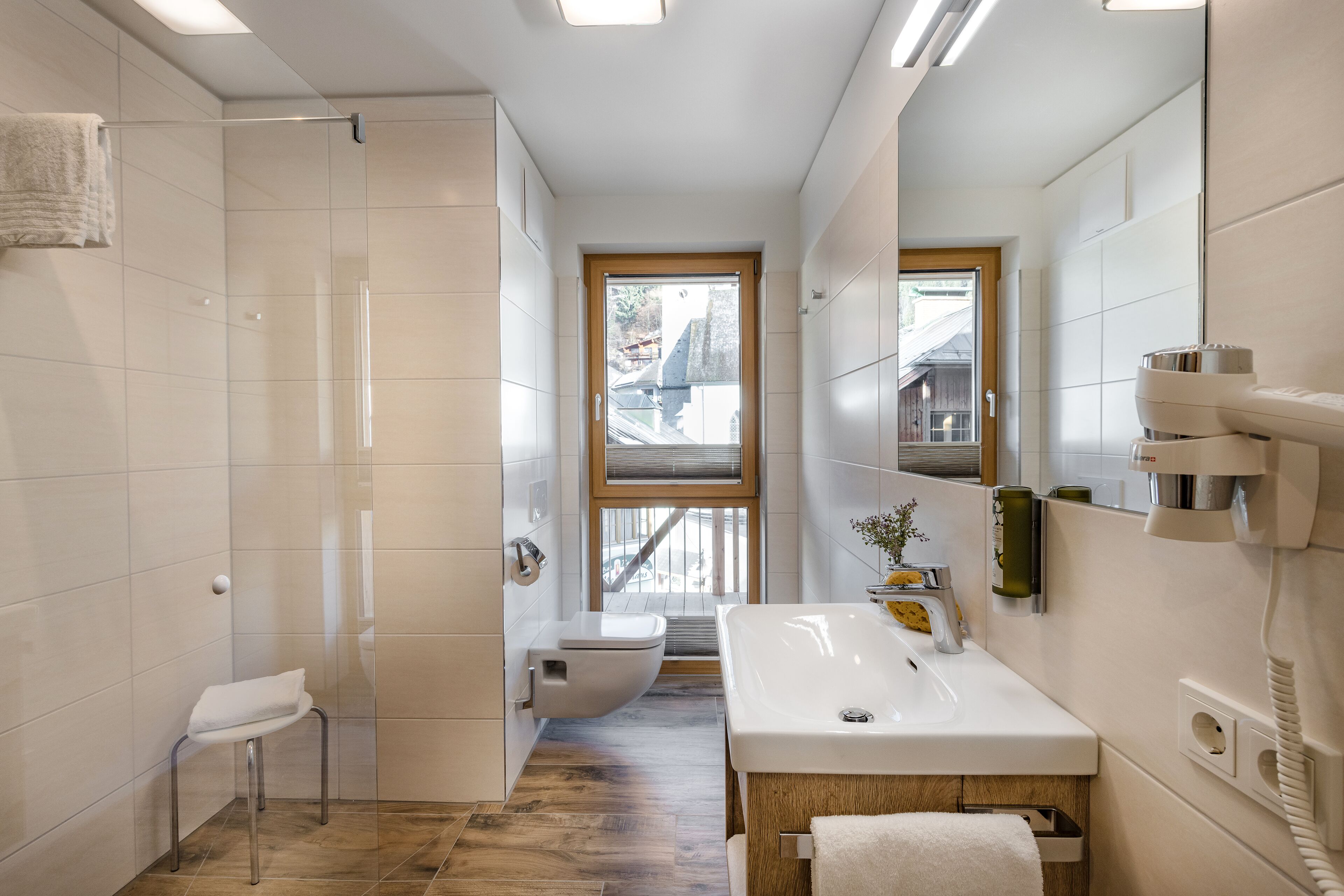A modern bathroom with a glass shower enclosure, a toilet, a sink with a mirror, and a wooden floor.