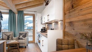 A cozy kitchen with wooden cabinets, a dining area with a table, and a view of the mountains through large windows. - AlpenParks Hotel & Apartment Hochkönig (Muehlbach Am Hochkoenig)