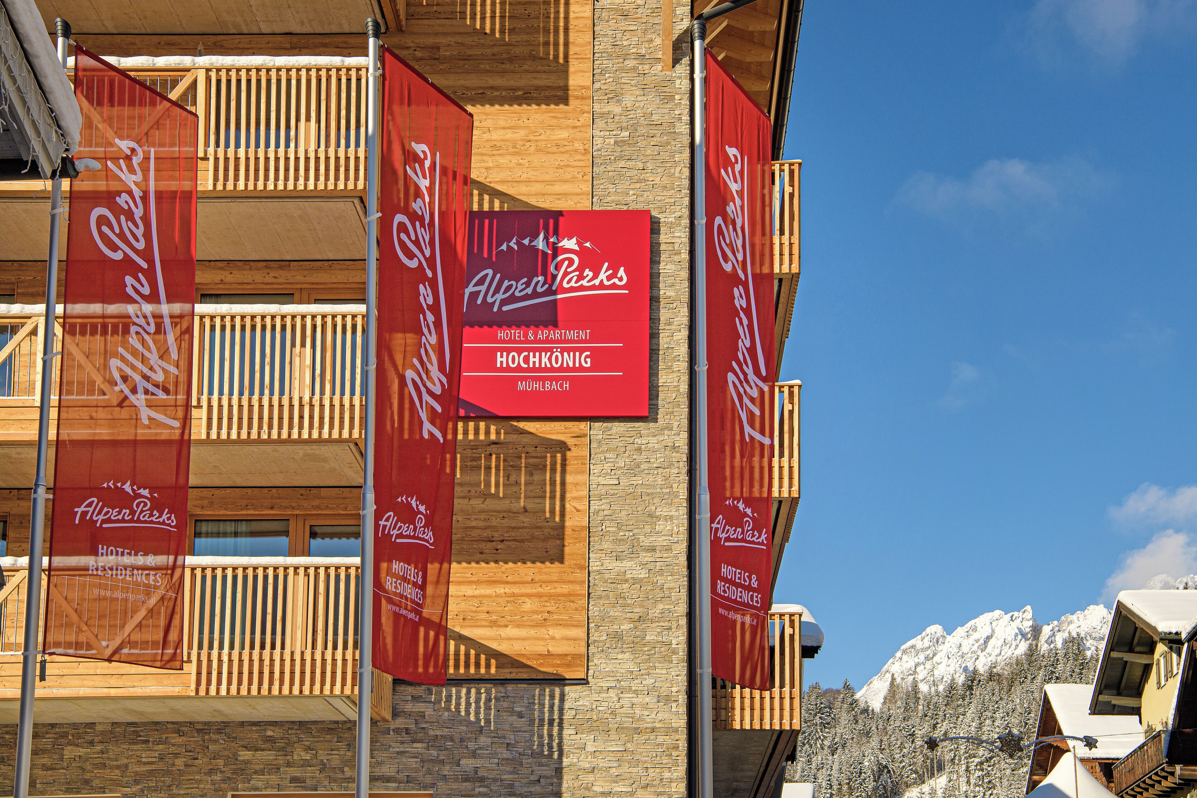 Un hotel con varias pancartas rojas, balcones y una montaña nevada al fondo.