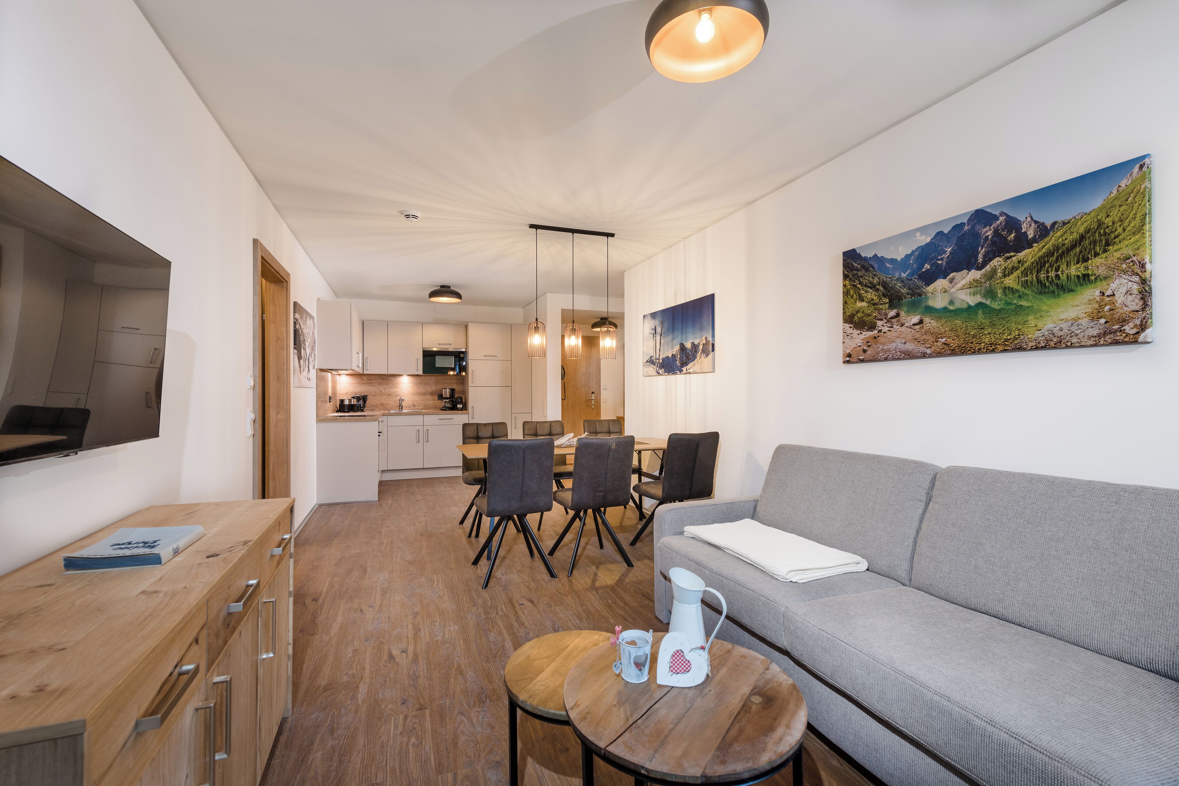 A modern living room with a grey sofa, wooden coffee table, and a dining area with chairs and a table.