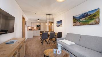 A modern living room with a grey sofa, wooden coffee table, and a dining area with chairs and a table.