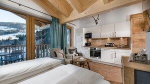 A modern room with a large window, a cozy seating area, a kitchenette, and a wooden ceiling. - AlpenParks Hotel & Apartment Hochkönig (Muehlbach Am Hochkoenig)