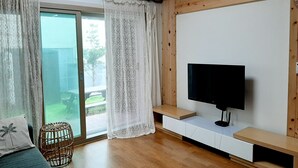 Ein modernes Wohnzimmer mit großem Fernseher, Holzboden und einer Schiebeglastür, die zu einem Außenbereich führt.