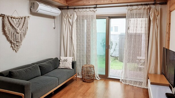 Ein gemütliches Wohnzimmer mit einem grauen Sofa, einem gewebten Hocker und einem Fernseher auf einem Holzboden.