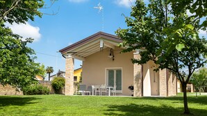 Ein Haus mit überdachter Terrasse, Grill und Rasen.