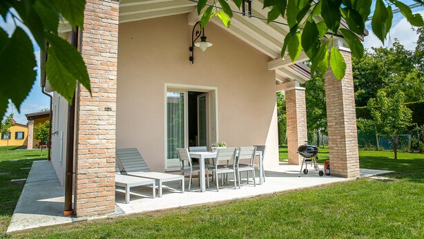 Eine überdachte Terrasse mit Tisch, Stühlen, einem Grill und einer Ziegelwand.