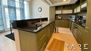 A modern kitchen with dark green cabinets, a black countertop, and a stainless steel sink. - Stylish 1 Bed apartment in Downtown Dubai (Dubai)