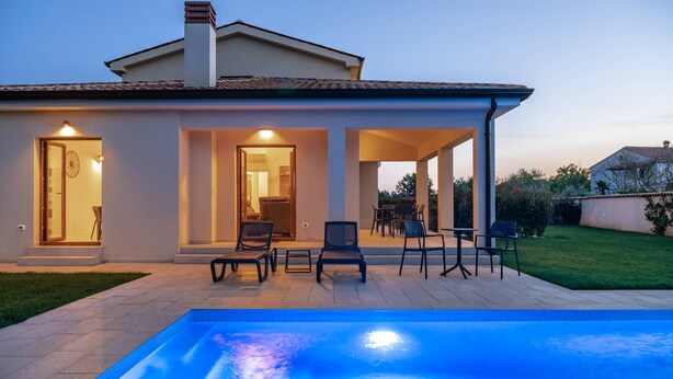 A modern house with a swimming pool, outdoor seating, and a well-lit patio area.