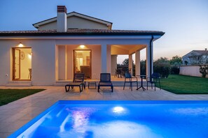 Una casa moderna con piscina, area salotto esterna e patio ben illuminato.