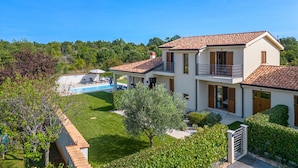 A two-story house with a swimming pool, surrounded by greenery and a clear blue sky.
