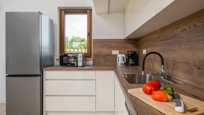 A modern kitchen with a stainless steel refrigerator, a wooden countertop, a sink, and a window with a view of greenery.