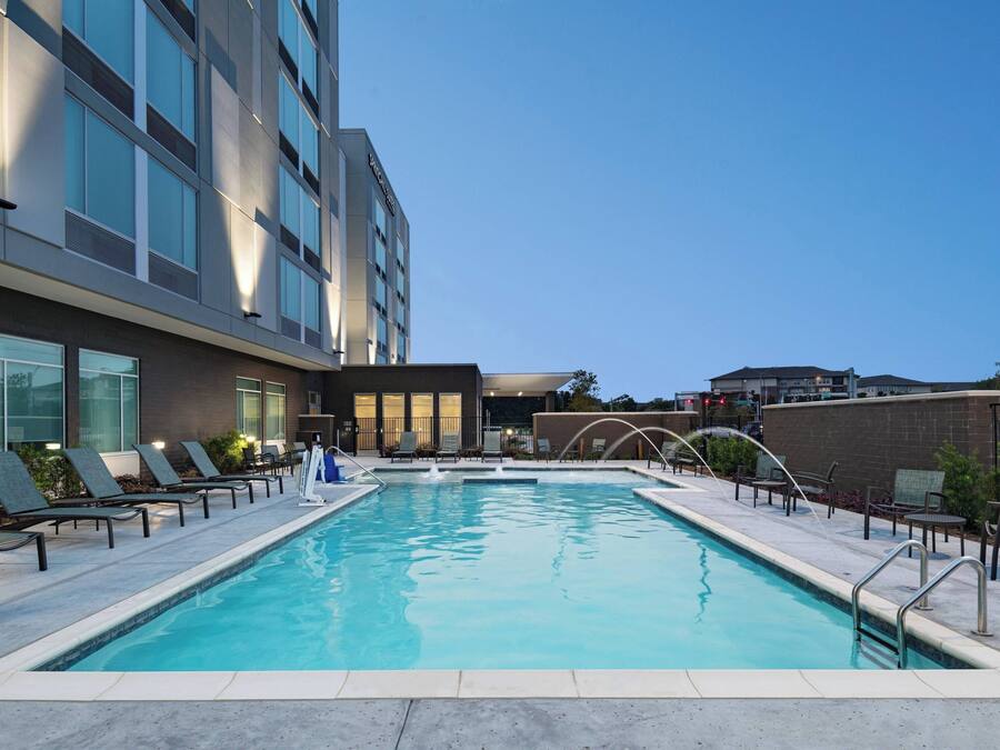 A swimming pool with lounge chairs and a building with large windows.