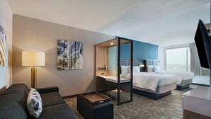 Ein Hotelzimmer mit einer Couch, einem Schreibtisch, einem Bett und einem großen Fenster.