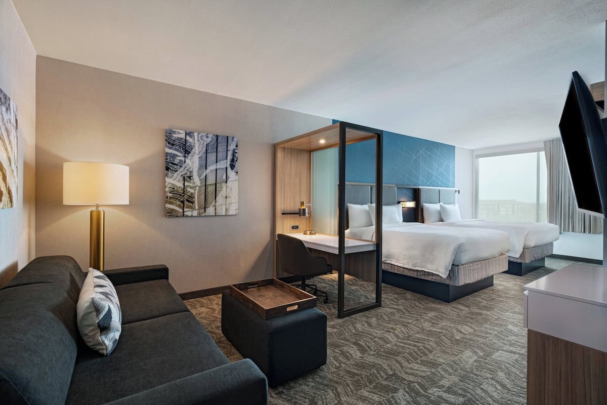 A hotel room with a sofa, a desk, a bed, and a large window.