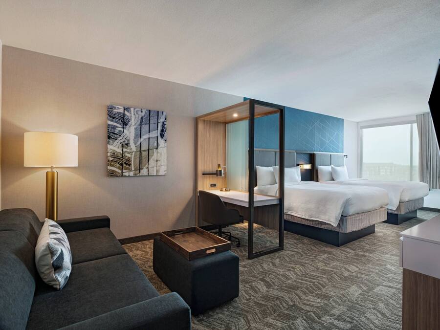 A hotel room with a sofa, a desk, a bed, and a large window.
