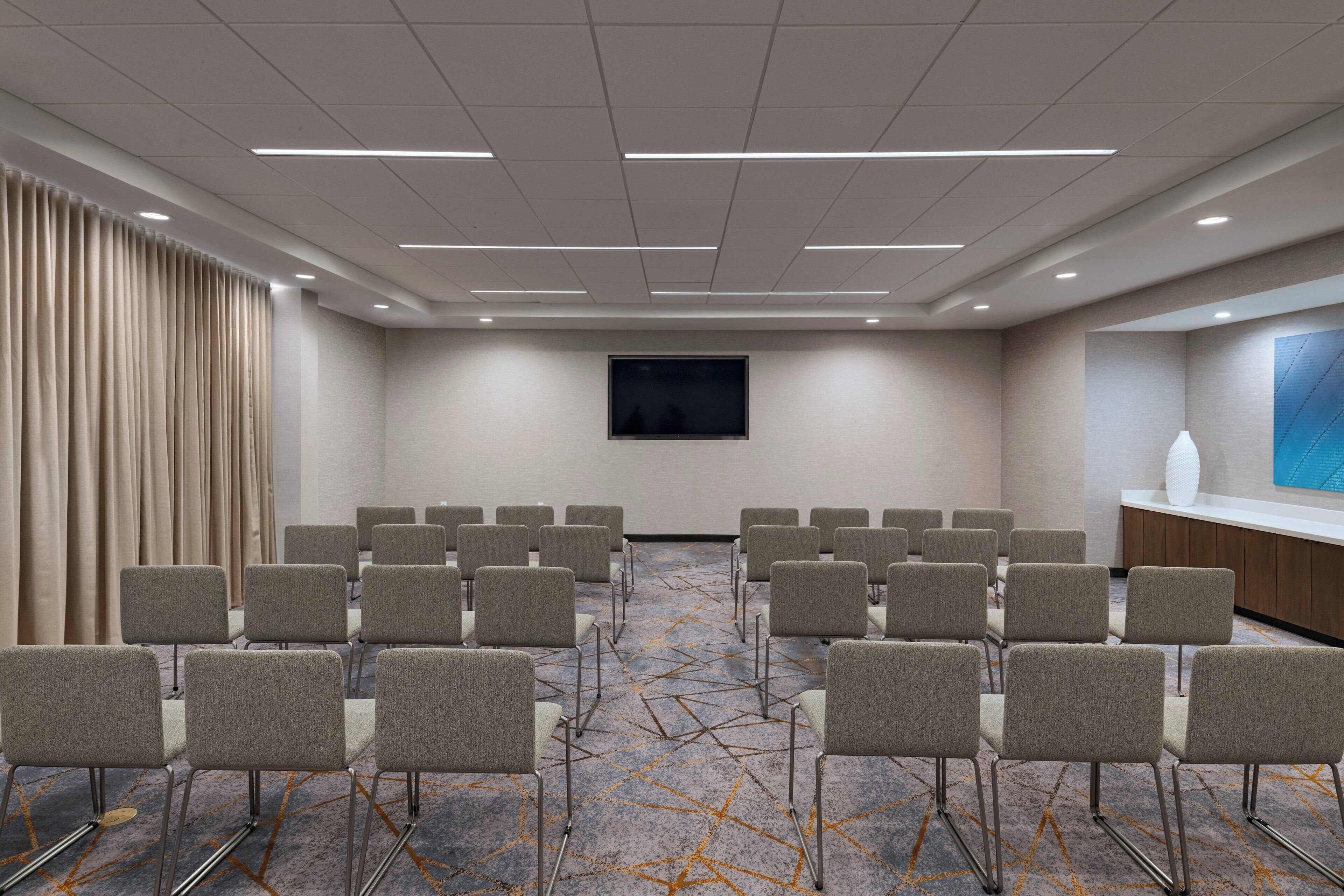 Un salón de conferencias con filas de sillas, un televisor de pantalla plana y piso alfombrado.