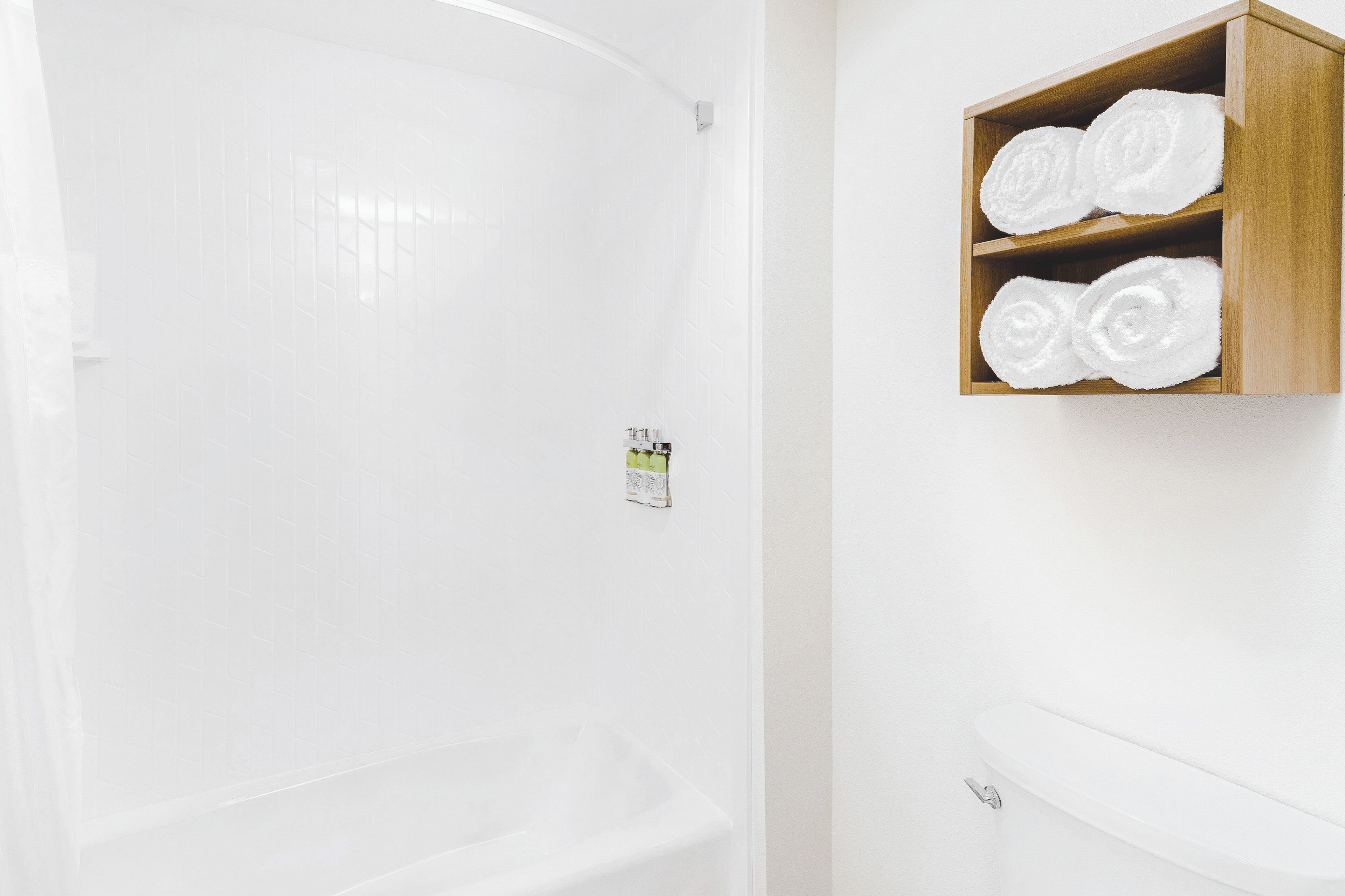 A bathroom with a white bathtub, a wooden shelf with rolled towels, and a small sign on the wall.