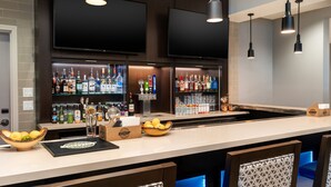 Una zona de bar con una barra larga, varias botellas de licor, vasos y un televisor montado en la parte superior.