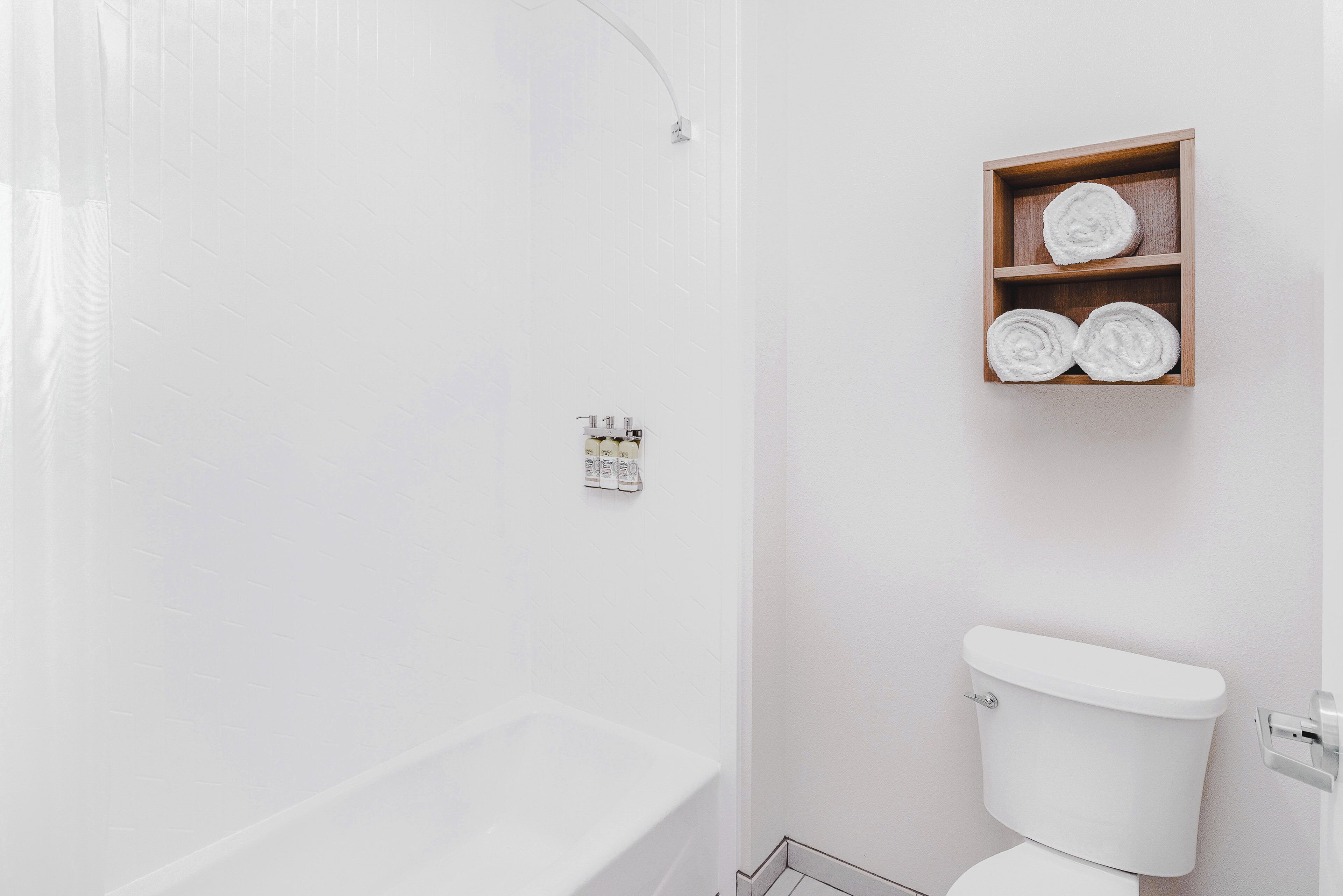 Une salle de bain avec une baignoire blanche, des toilettes et une étagère en bois où sont pliés des serviettes.