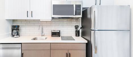 Una cocina moderna con armarios blancos, un refrigerador de acero inoxidable, un microondas, una cafetera y un tostador.