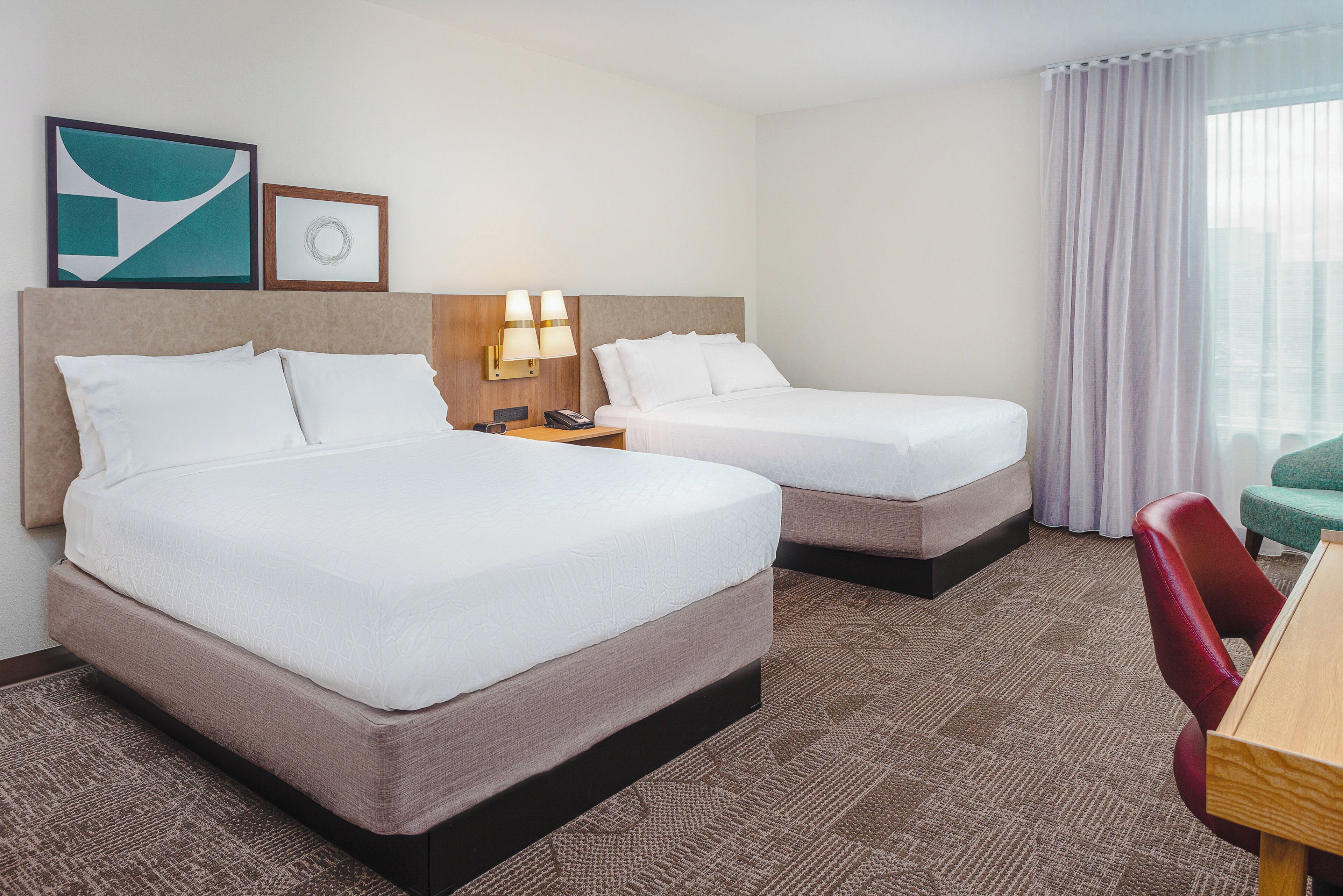A hotel room with two beds, a desk, a chair, and a window with curtains.