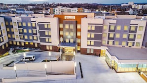 Un hotel de varios pisos con entrada central, zona de estacionamiento y vistas del barrio circundante.