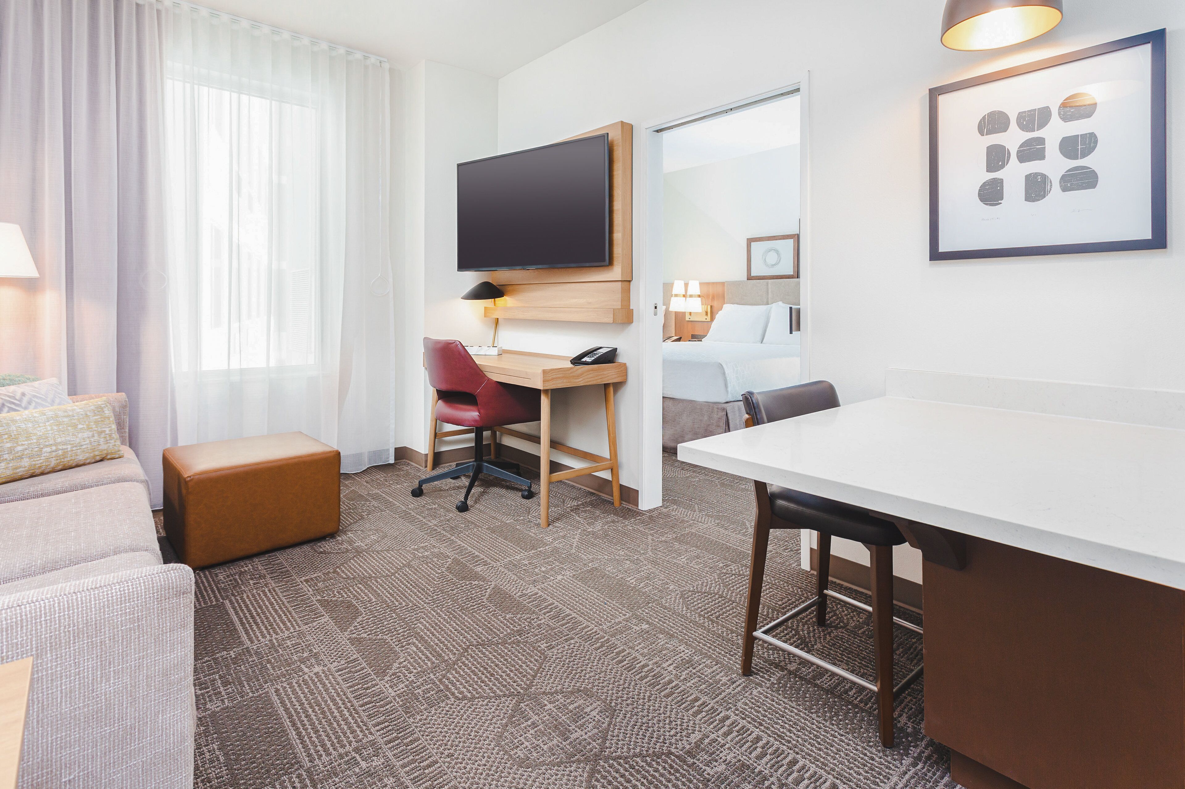 Een hotelkamer met een bed, een bureau, een stoel, een televisie en een ingelijste foto aan de muur.