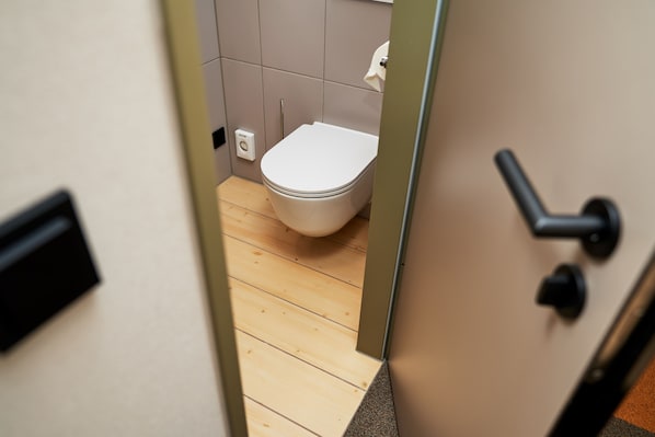 Een uitzicht door een deur naar een badkamer met een houten vloer, een wit toilet en een handdoekdispenser.