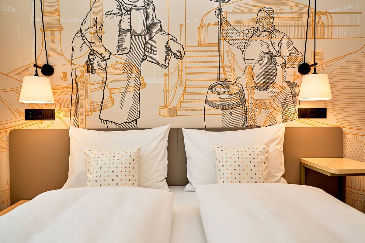 Une chambre d’hôtel avec un grand lit, deux tables de chevet et une fresque murale représentant des chefs.