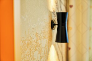 Ein Detailaufnahme einer Wand mit strukturierter Oberfläche und einem daran befestigten schwarzen Objekt, möglicherweise einer Leuchte.