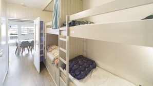 A bunk bed room with a desk and chairs, a window, and a door leading to another room.