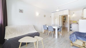 A modern living room with a sofa, a dining table with chairs, a small table, and a bed.