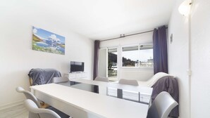 A modern room with a dining table, chairs, a TV, and a window with curtains.