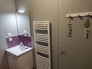 A bathroom with a white sink, a mirror, a towel rack, and a door with a towel hanging.