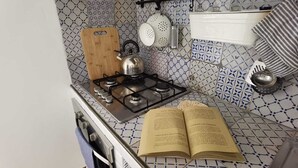 Cucina con piano cottura a gas, bollitore, tagliere e un libro sul bancone.